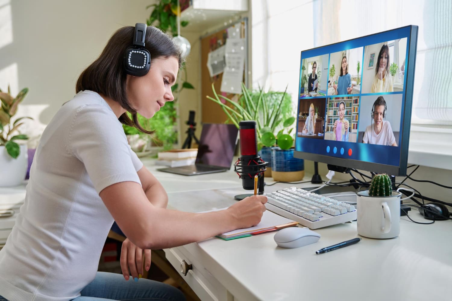 Person taking notes at a desk while joining a live virtual training session on a monitor