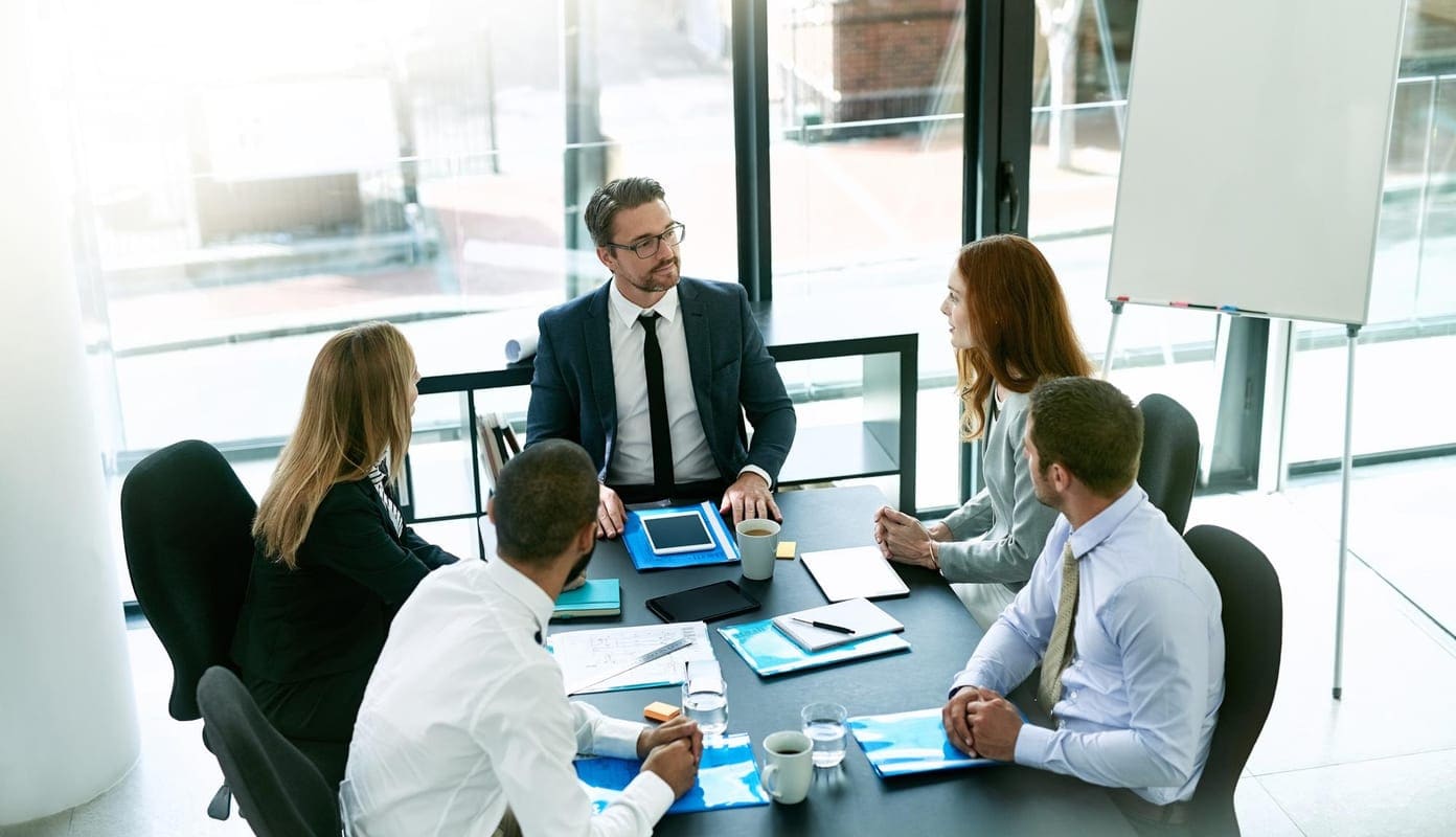 Colleagues around a boardroom table reviewing tablets during a working session