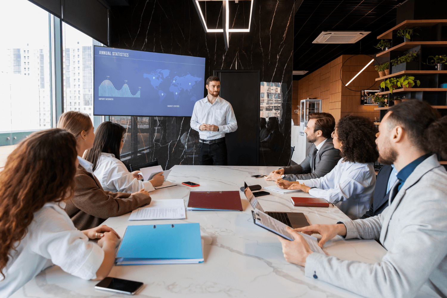 Presenter briefing colleagues around a table in front of a data dashboard