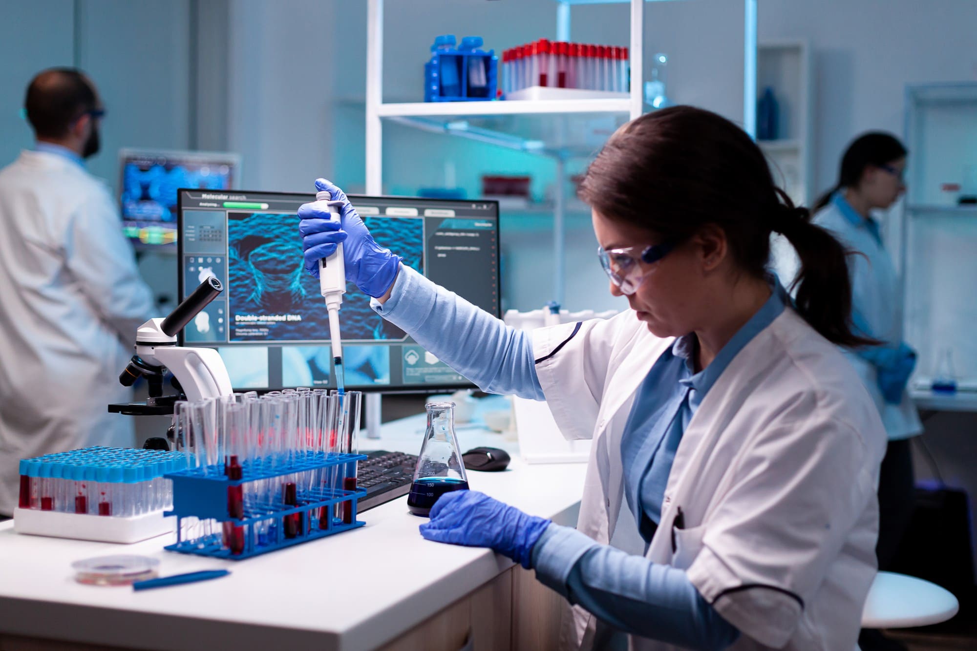 Laboratory scientist pipetting samples beside a monitor in a pharma lab